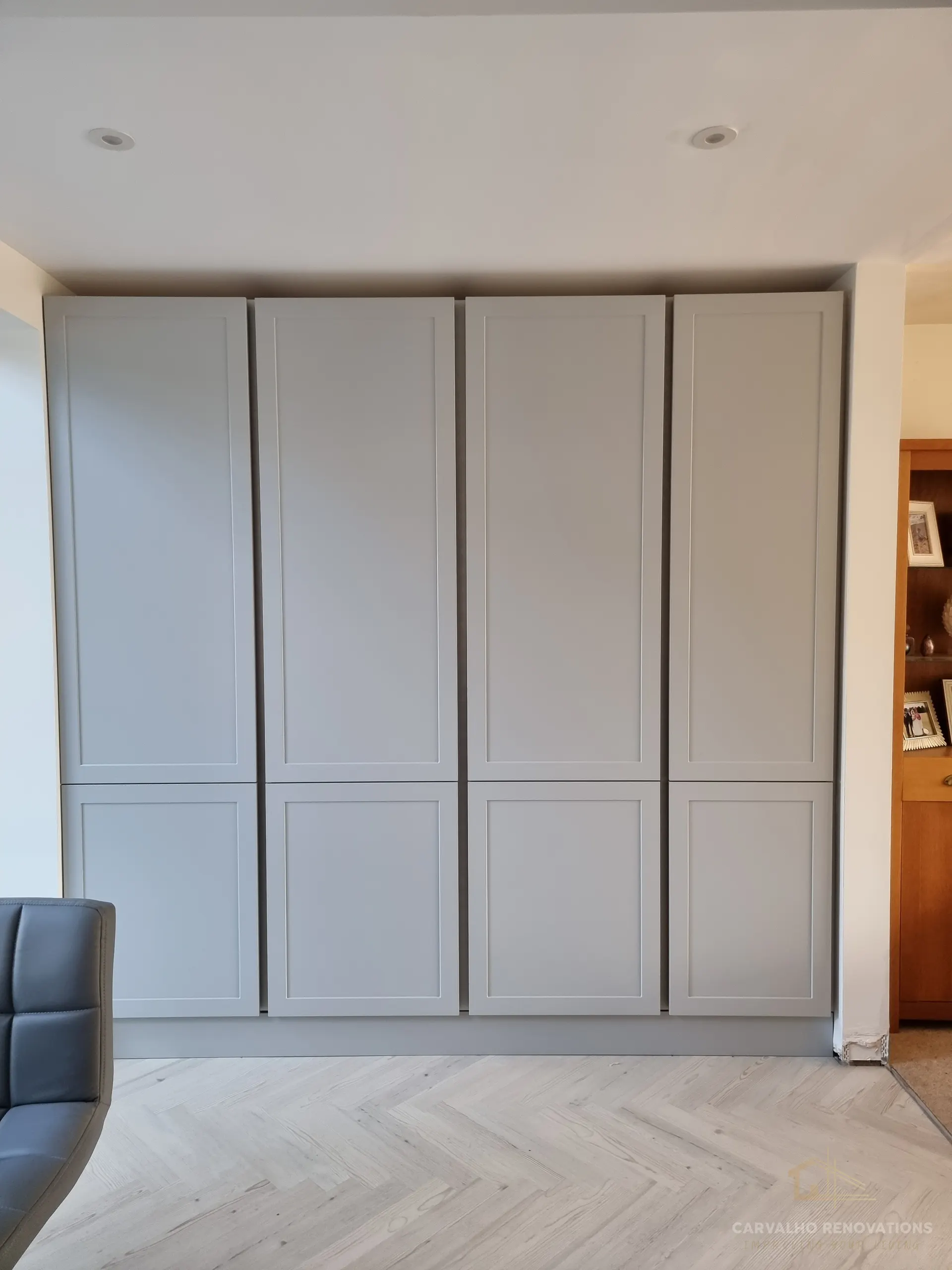 Run of four full-height light grey Shaker doors providing floor-to-ceiling storage, on herringbone flooring.