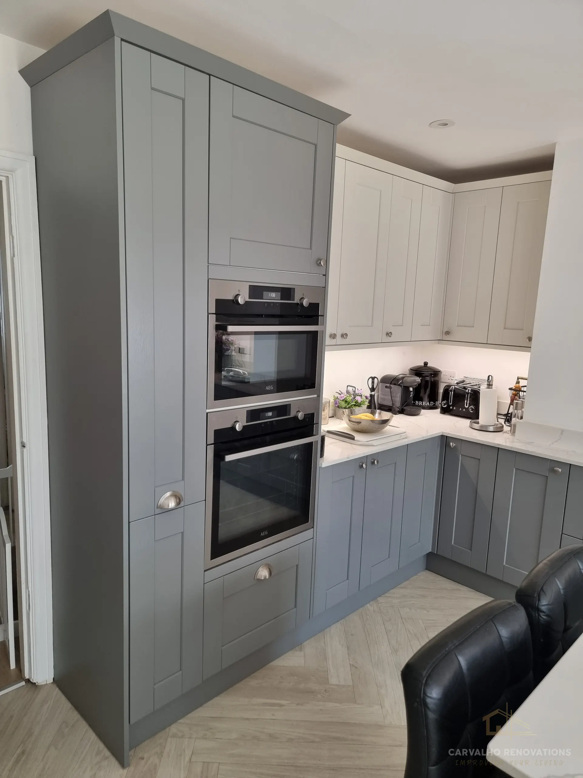 Tall grey Shaker unit housing a built-in double oven, next to light wall cabinets and a marble-effect worktop.