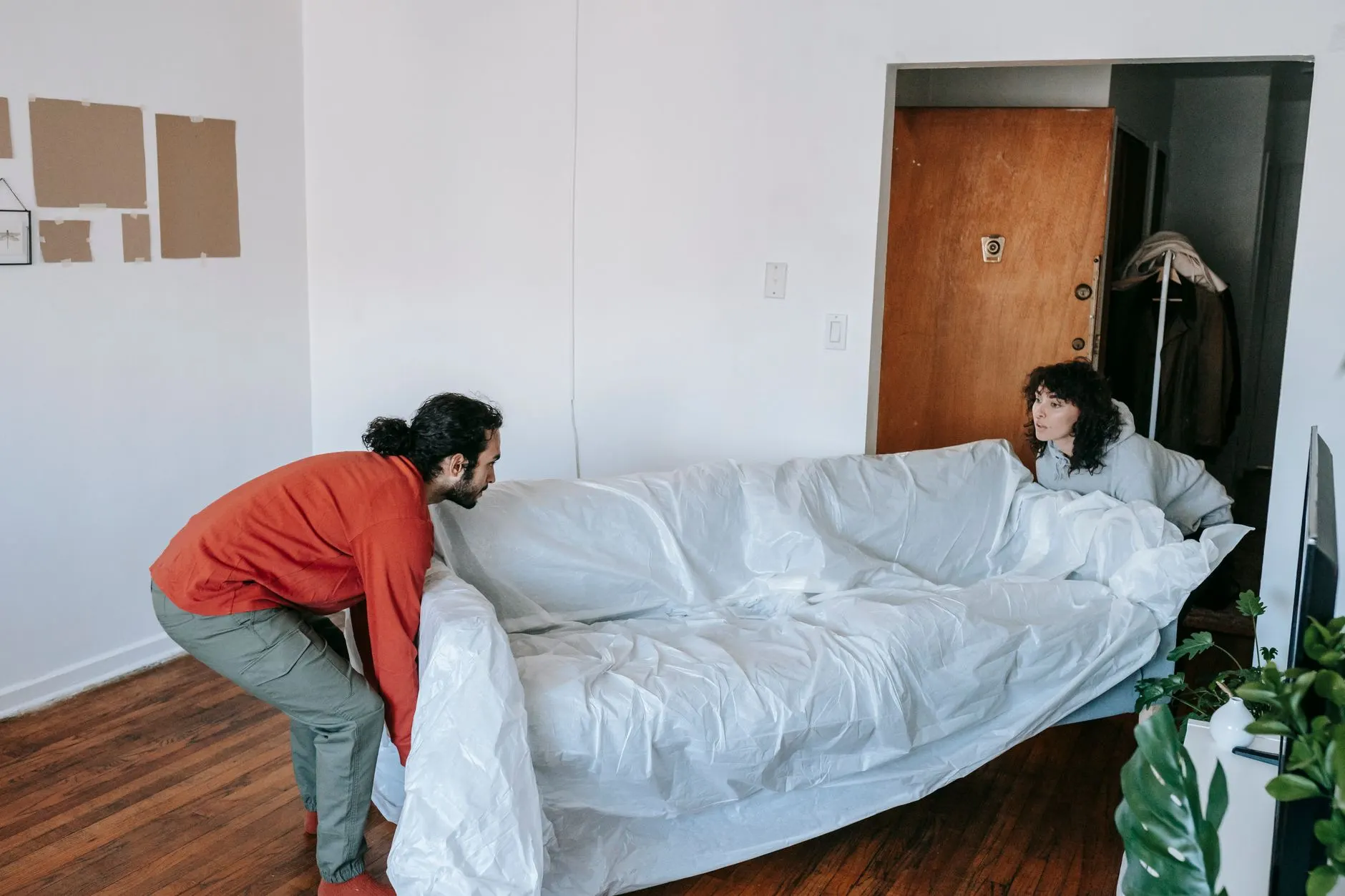 A couple collaboratively lifting a couch while moving into a new apartment.