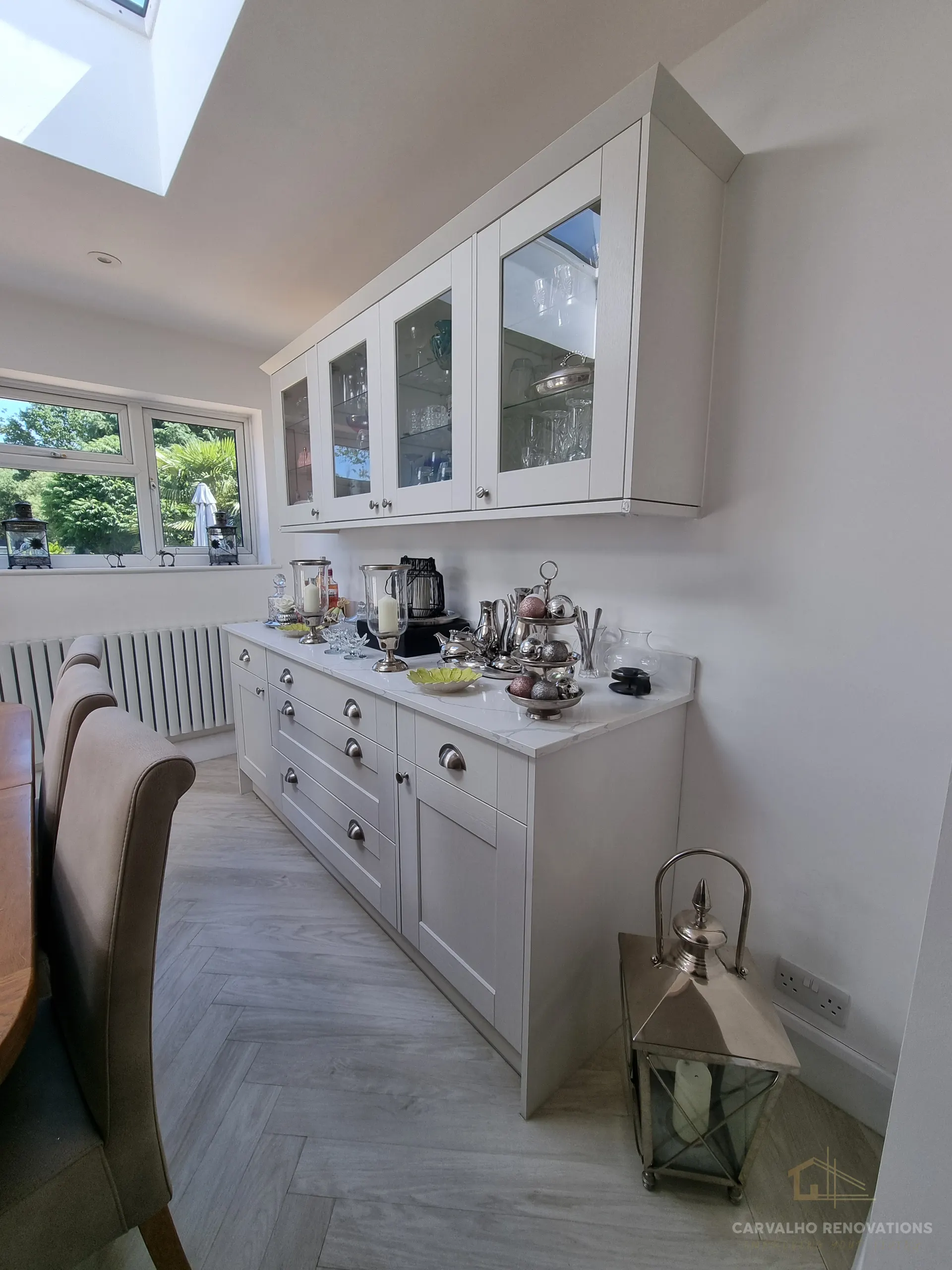 Light Shaker dresser run with glazed wall cabinets, cup handles and a marble-effect worktop, alongside the dining table.