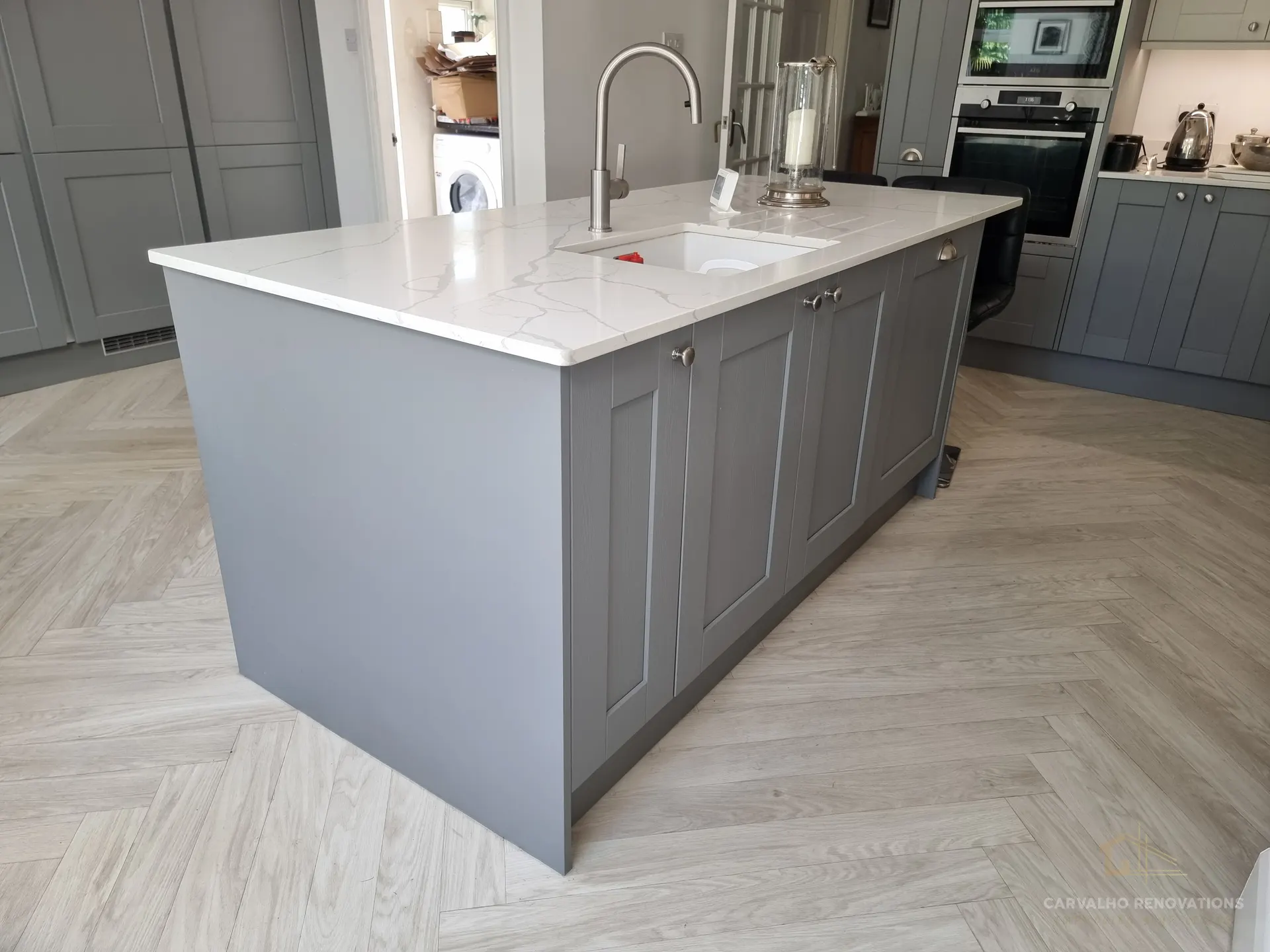 Kitchen island from the side, showing an undermount sink, veined quartz-effect worktop and grey Shaker doors.