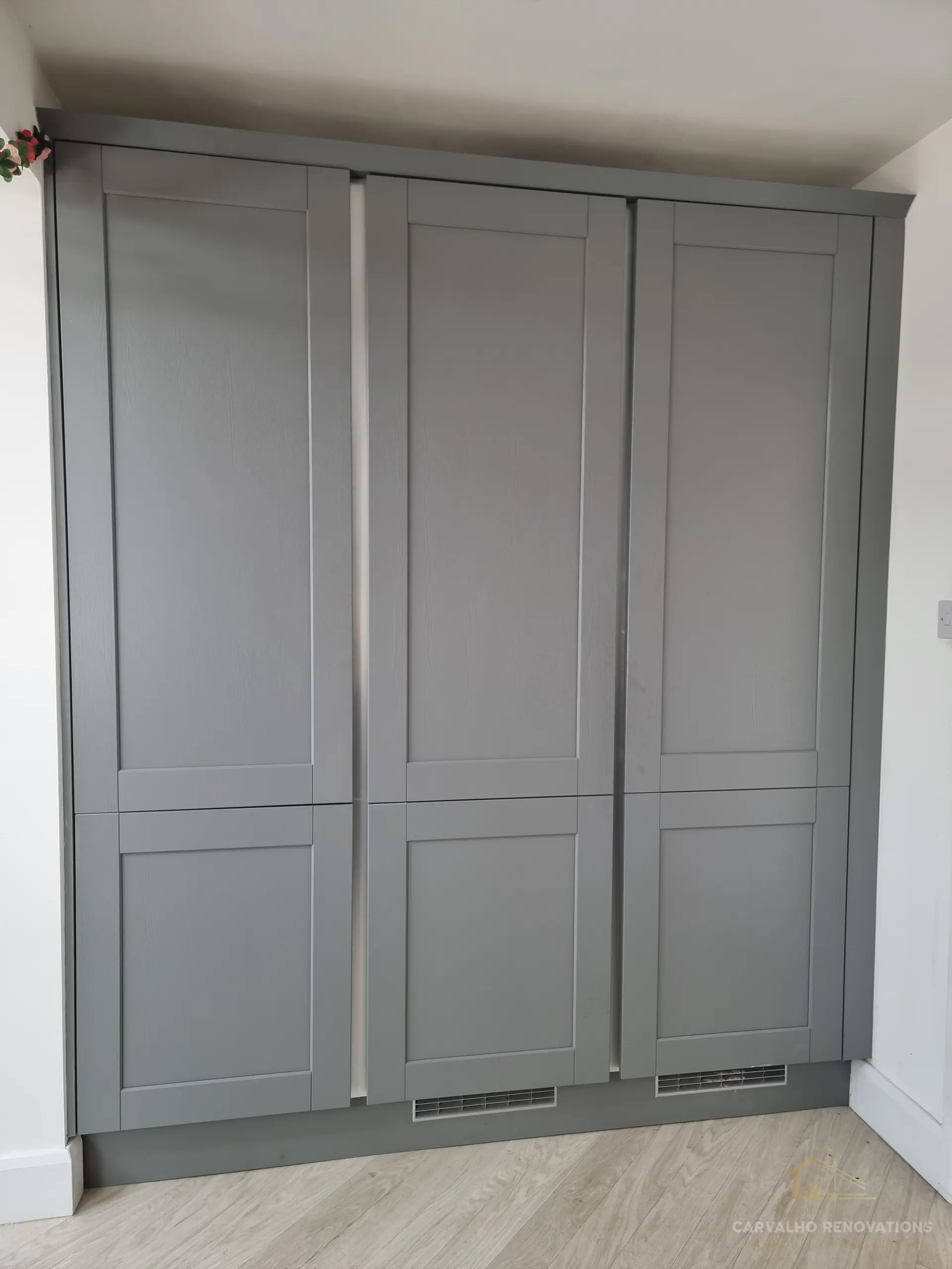 Bank of full-height grey Shaker cabinets finished with cornice and a plinth with ventilation grilles.
