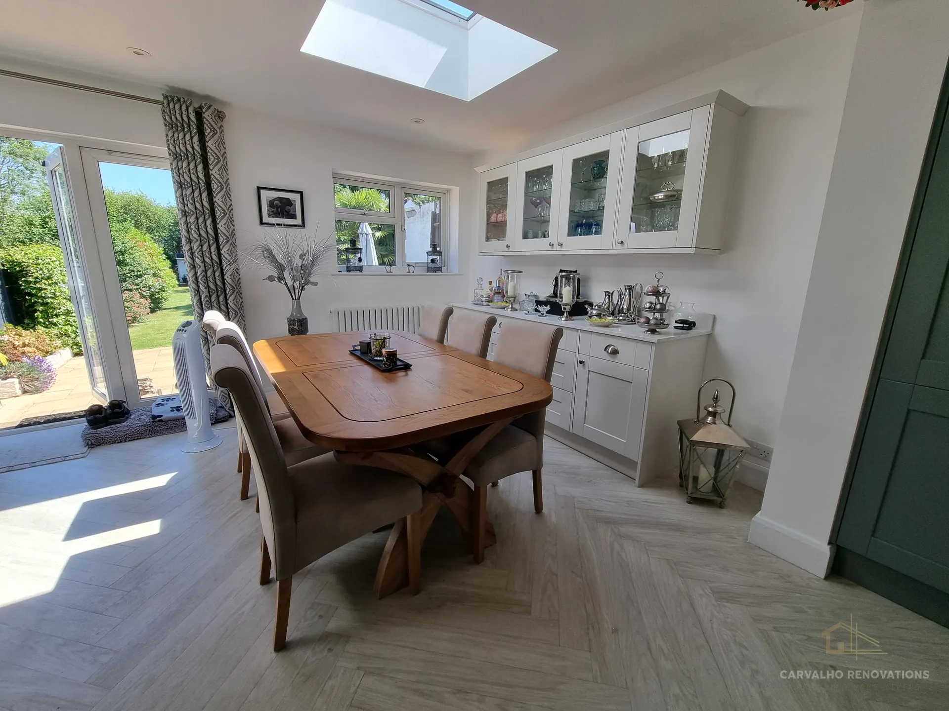 Dining area beside the kitchen, with light Shaker wall cabinets with glazed doors, a marble-effect worktop run, a skylight and French doors onto the garden.